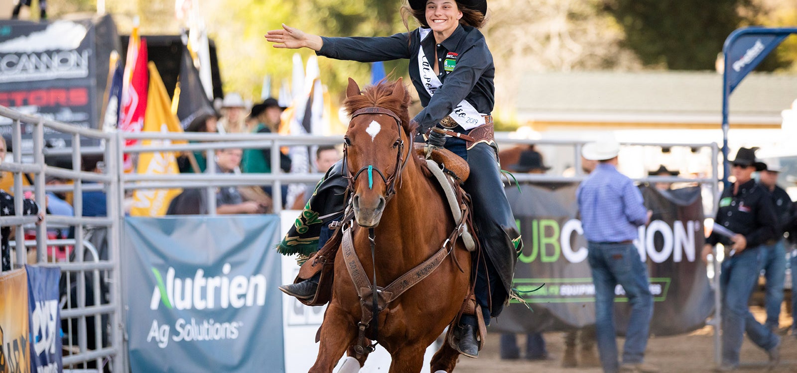 A smiling cal poly rodeo team member rides a horse a horse in the arena