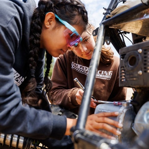 Two students make on-the-spot repairs of the baja vehicle during a testing session.