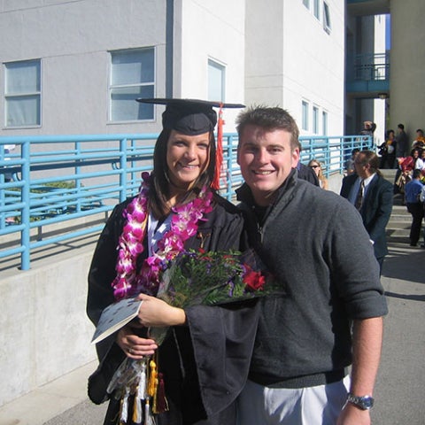 Cal Poly couple posing together in front of a white building in their graduation regalia.