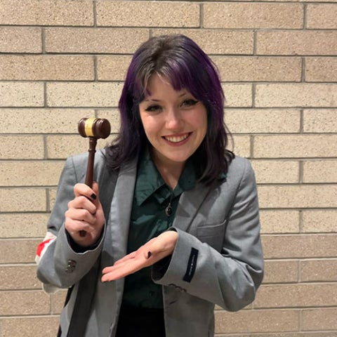 Student holding up a gavel while wearing professional business attire.