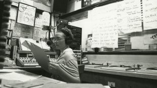 A KCPR DJ looks at a clipboard inside the recording studio.