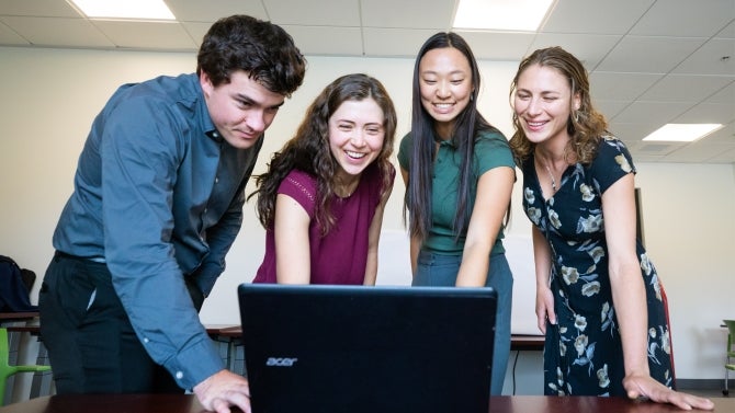 Four students happily gather around laptop