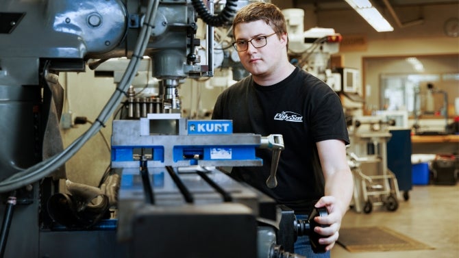 Student operating industrial equipment wearing a black t-shirt and protective glasses