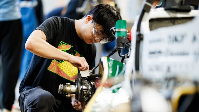 Student in black t-shirt working on mechanical equipment for Cal poly's race car.