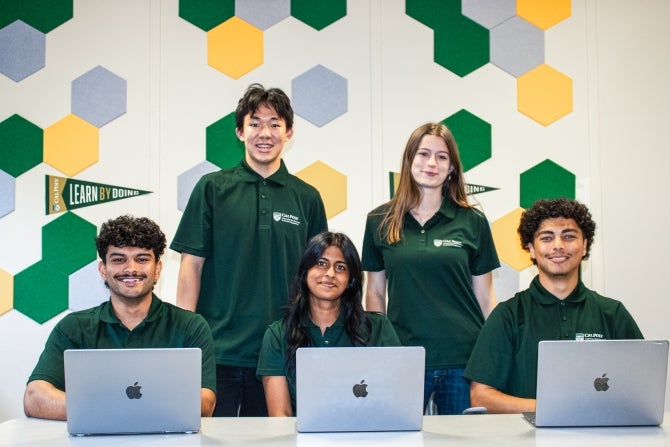 Group of diverse college students posing together behind laptops.
