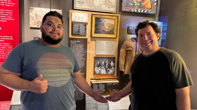 Two men stand in front of a gallery of historical images.