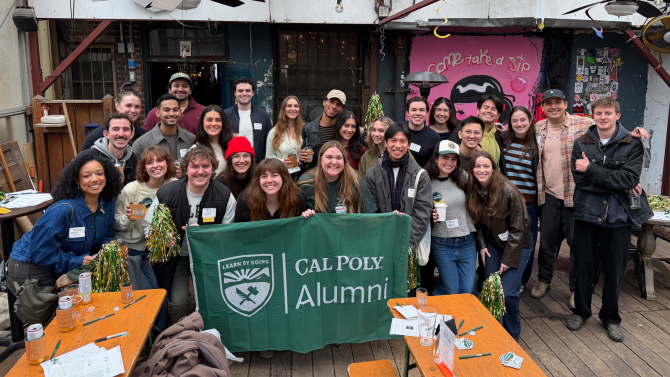 A group of people smiling with a banner in front that reads 'Cal Poly Alumni'