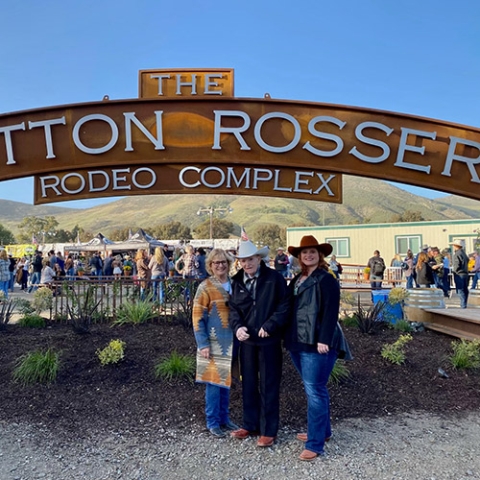 Cotton Rosser, wearing a cowboy hat, stands with two companions under the new Cotton Rosser Rodeo Complex entrance sign