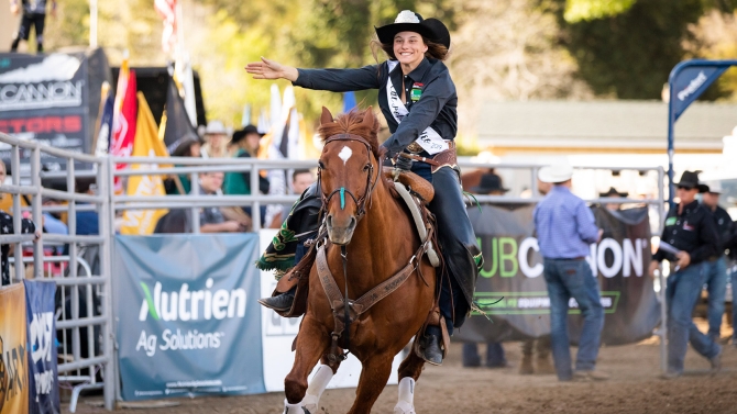 A smiling cal poly rodeo team member rides a horse a horse in the arena