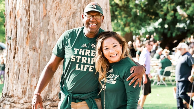 Alumni couple wearing Cal Poly gear, smiling for the camera.